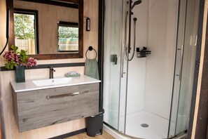 A modern bathroom with a wooden vanity, a glass shower enclosure, and a window providing natural light.