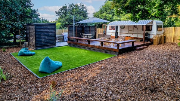 A backyard with a picnic table, two bean bags, a small shed, and a camper parked in the background.