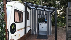 Een recreatiewoning met een kitchenette, inclusief een spoelbak en kastjes, en een overdekte buitenruimte met een houten terras.