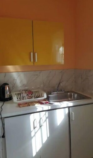 A compact kitchen with white cabinets, a sink, and a kettle on the countertop.