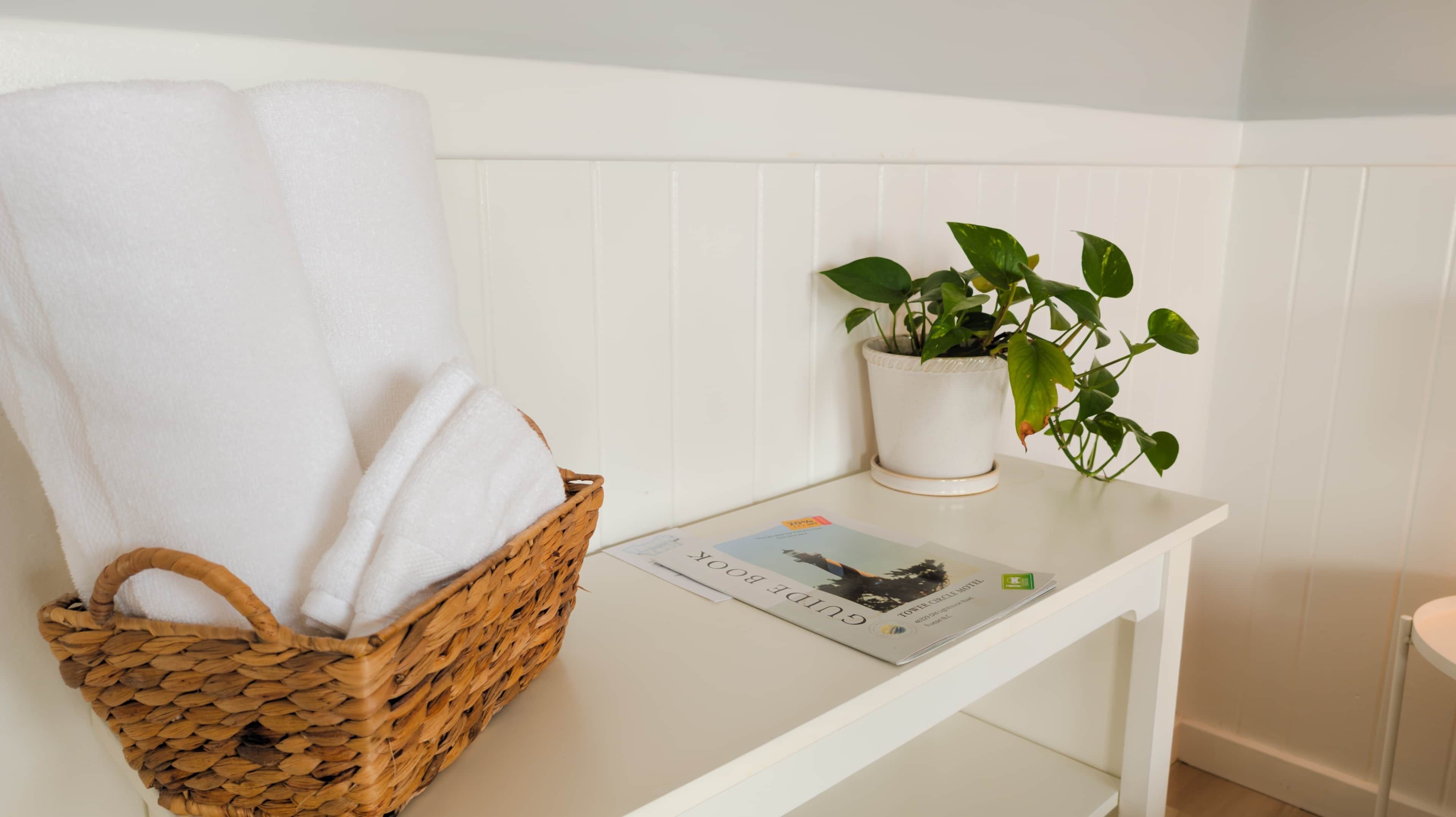 A white shelf with a woven basket holding white towels, a potted plant, and a magazine.