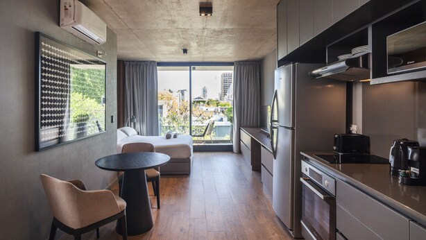 Una cocina moderna con horno integrado, refrigerador y cafetera. Hay un comedor con una mesa redonda y dos sillas.