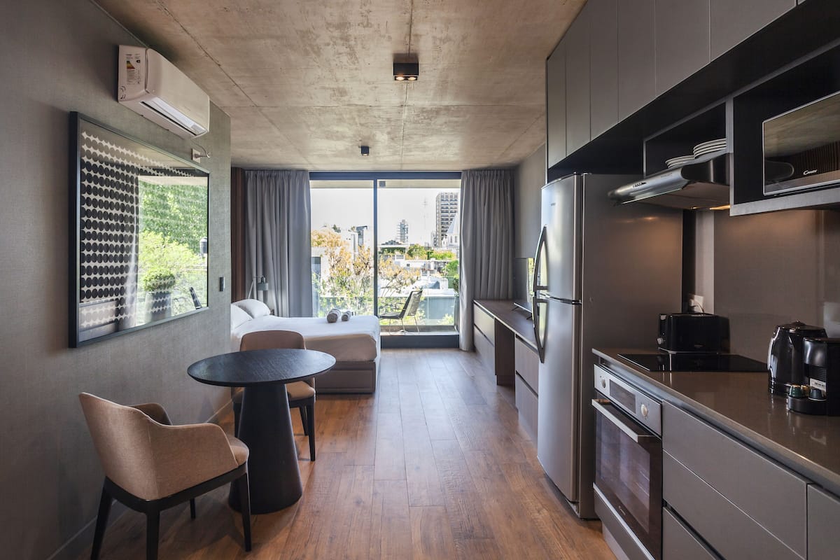 Una cocina moderna con horno integrado, refrigerador y cafetera. Hay un comedor con una mesa redonda y dos sillas.