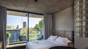 Una habitación de hotel moderna con una cama grande, una mesa redonda y un balcón con vistas a la ciudad.