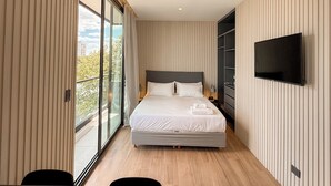 Un dormitorio moderno con una cama grande, un televisor montado en la pared y un balcón con vistas a la ciudad.