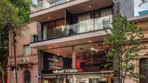 Un edificio de varios pisos con fachada de vidrio, un local comercial con señalización y una entrada visible.