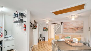 A modern kitchen with white cabinets, a stove, and a black pot rack. There is a dining area with a wooden table and chairs, and a painting on the wall. - Epic Brunswick Apartment with Hot Tub! (Brunswick)