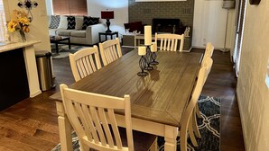 A dining area with a wooden table and chairs, a fireplace, and a sofa in the background.