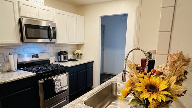 A kitchen with white cabinets, a stainless steel sink, a microwave, a stove, and a coffee maker.
