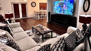 A living room with a large flat-screen TV, a ceiling fan, and a dining area with a table and chairs.