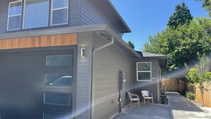 A modern two-story house with a garage, a covered patio with chairs, and a wooden fence. - New Guest Suite 2br/1bth in DT Vancouver - pet friendly (Vancouver)