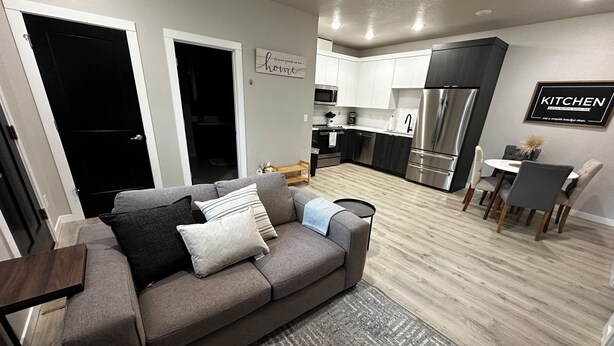 A modern living room with a grey sofa, a dining area with a round table and chairs, and a kitchen with stainless steel appliances. - New Guest Suite 2br/1bth in DT Vancouver - pet friendly (Vancouver)