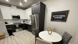 A modern kitchen with white and dark cabinets, stainless steel appliances, and a dining area with a white table and grey upholstered chairs. - New Guest Suite 2br/1bth in DT Vancouver - pet friendly (Vancouver)