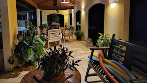 Un patio al aire libre con mobiliario de madera, plantas en macetas y un techo con vigas a la vista.