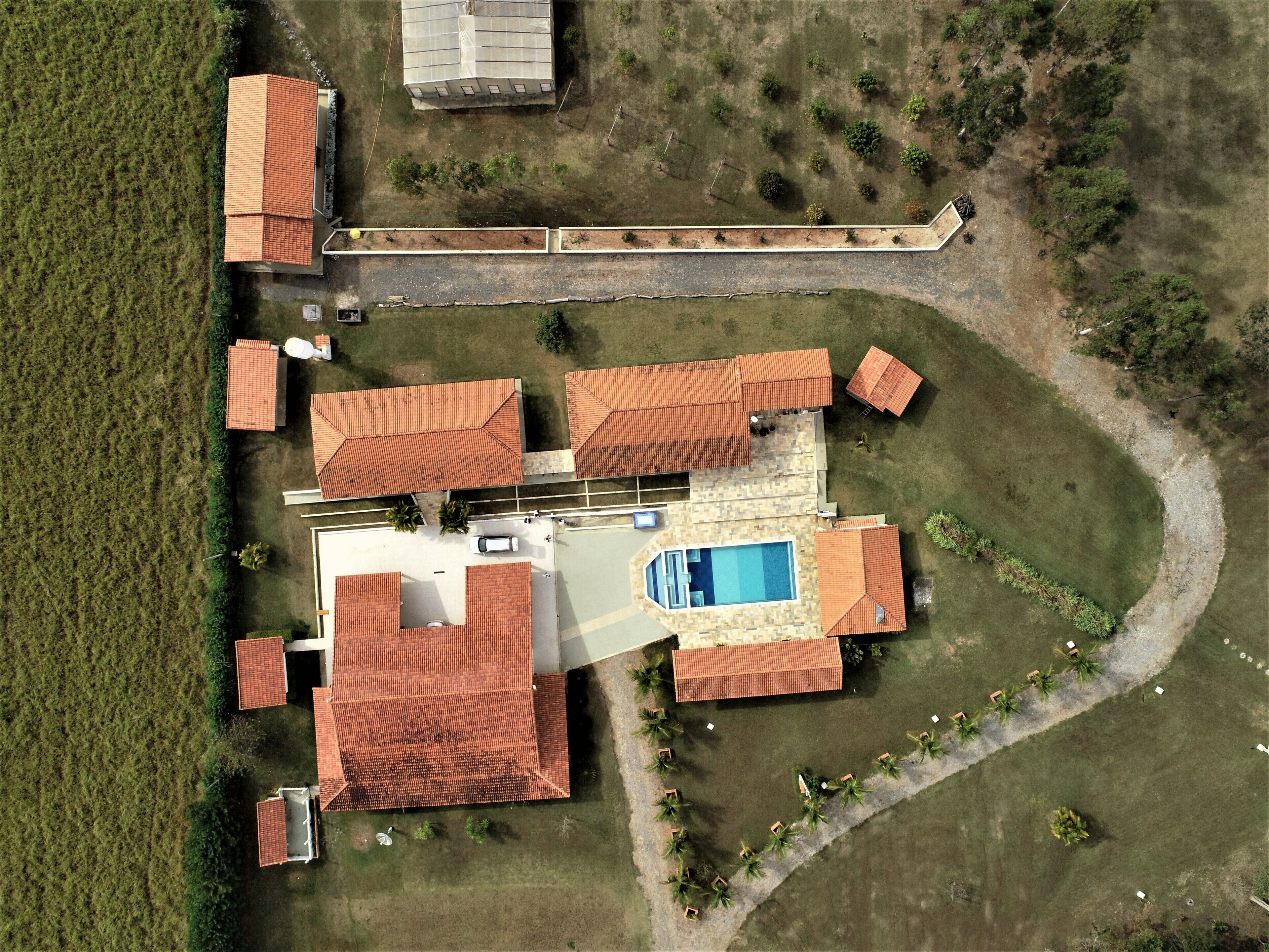 Una vista aerea di una proprietà residenziale con diversi edifici a tetti rossi, una piscina e un prato curato.