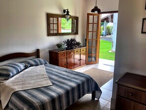 Un dormitorio con una cama, un aparador de madera, un espejo y una puerta que da a un jardín.