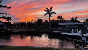A sunset over a residential area with houses, a dock, and a calm body of water reflecting the sky.