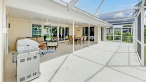 A spacious covered patio with a grill, seating area, and large windows offering views of the outdoors.