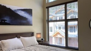 Een slaapkamer met een groot bed, een nachtkastje, een lamp en een raam met jaloezieën.