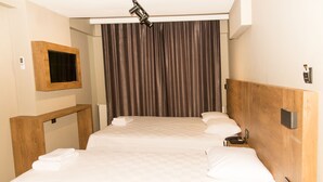 Camera d'albergo con due letti, una testiera in legno, una TV a parete e un'ampia finestra con tende.