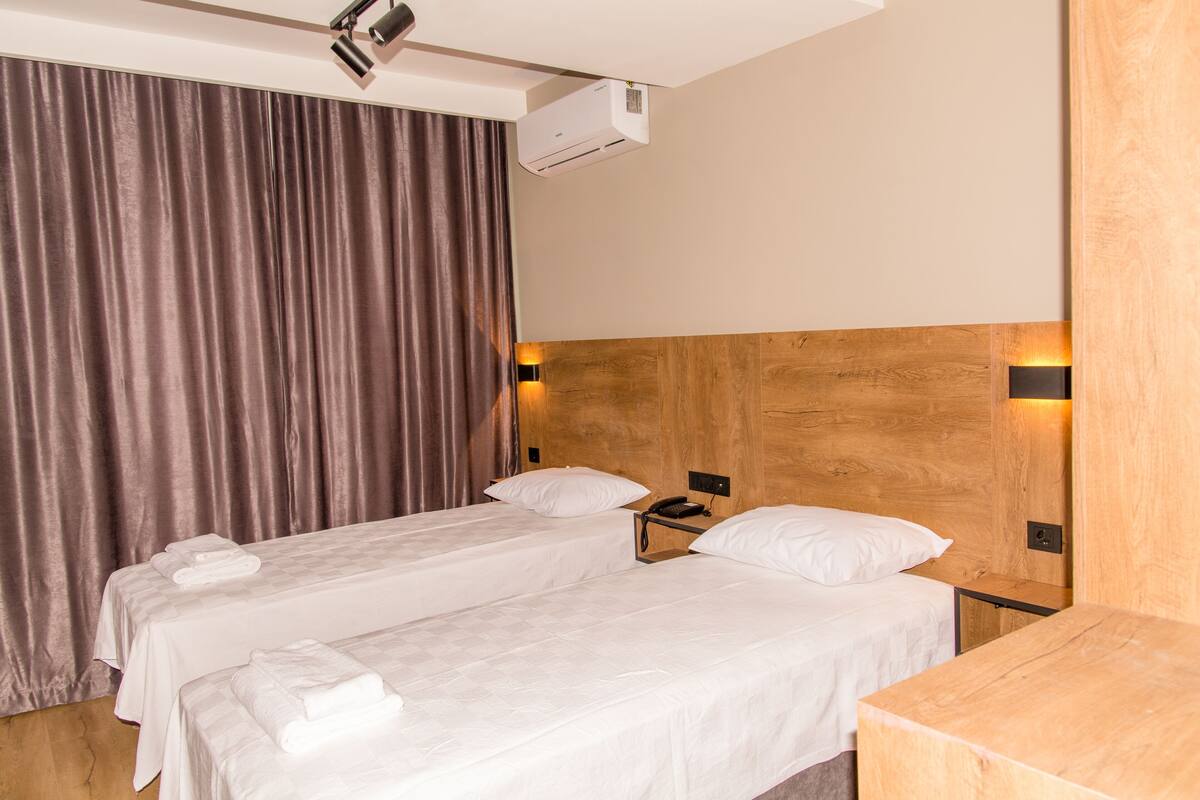 A hotel room with two beds, a wooden headboard, a telephone, and a wall-mounted air conditioner.