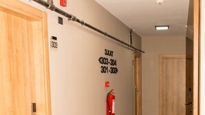 Un corridoio con porte in legno, un estintore e numeri di contatto di emergenza sulla parete.