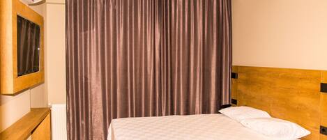 A hotel room with a wooden headboard, a bed with white linens, a large window with a view, and a wall-mounted air conditioner.