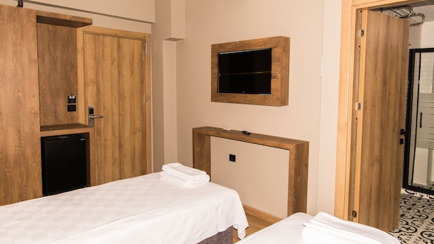 Una camera d'albergo con due letti, una TV a parete e un armadio in legno.