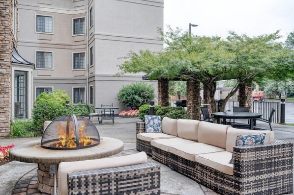 A patio with a fire pit, outdoor seating, and a building in the background.