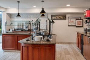 Une cuisine moderne dotée d’un îlot central, d’un buffet à vitrines et d’une pancarte indiquant que le petit-déjeuner est offert gratuitement chaque jour.