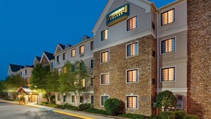 Un hotel de varios pisos con fachada de piedra, un cartel que indica 'Staybridge Suites' y una entrada bien iluminada.