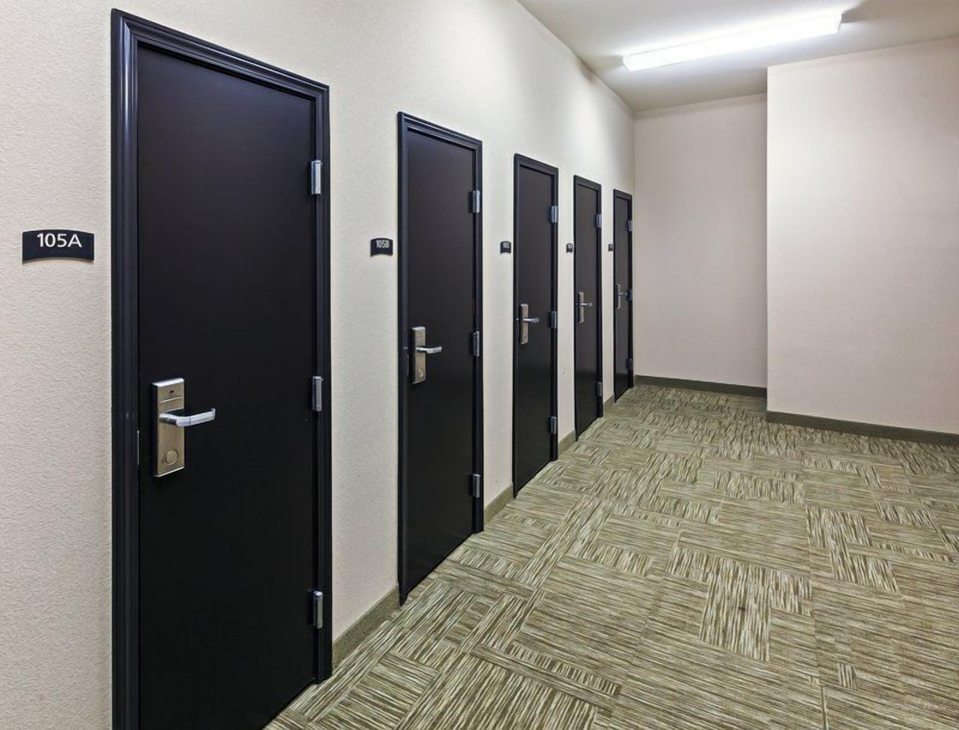 Un couloir avec des portes noires, chacune portant un numéro, qui donnent accès à des pièces individuelles.