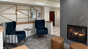 A modern lobby with two blue armchairs, a small side table, a fireplace, and a geometric wall design. - 1-Bedroom | Top Location | Pool, Hot Tub Access (West Des Moines)
