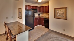 A kitchen with granite countertops, wooden cabinets, a refrigerator, and a dishwasher. - 1-Bedroom | Top Location | Pool, Hot Tub Access (West Des Moines)