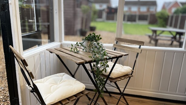 Ein Schlafsofa und ein Holztisch sind in einem Wintergarten mit großen Fenstern aufgestellt.