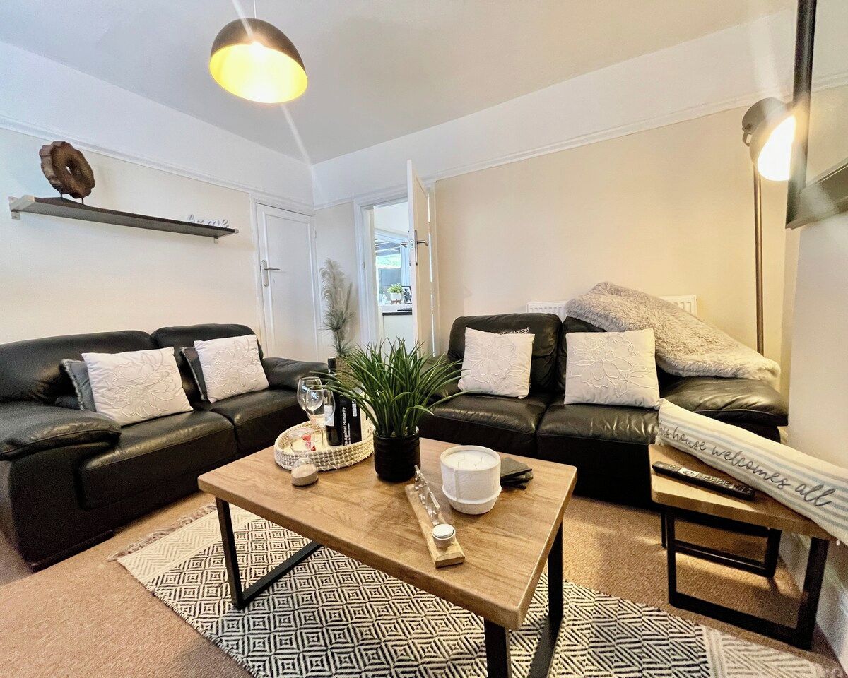 Ein modernes Wohnzimmer mit einem schwarzen Ledersofa, einem Holztisch und einem gemusterten Teppich.