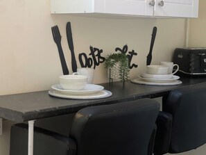 Eine Küchenarbeitsplatte mit zwei weißen Tassen und Untertellern, einer kleinen Topfpflanze und einem Toaster.