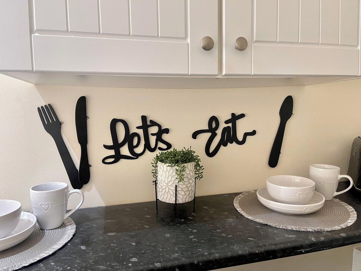Een aanrecht met een decoratief bord, keukengerei, een potplant en witte keramieken borden.