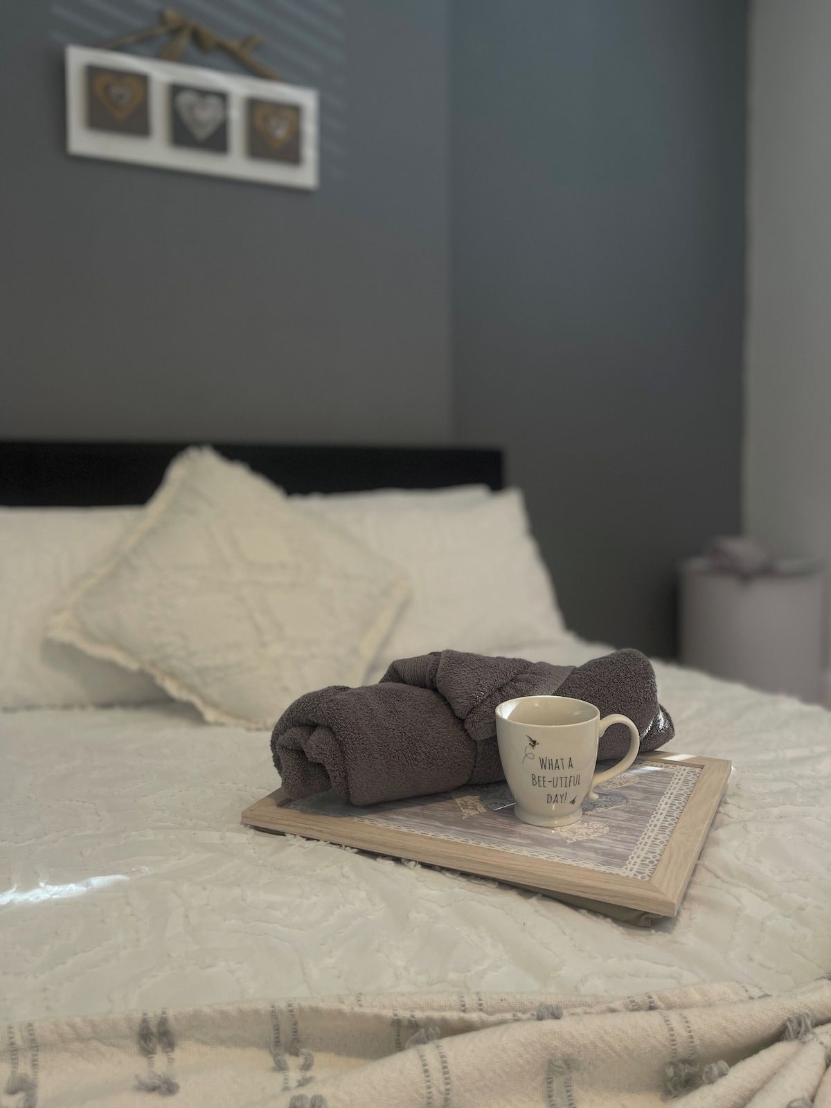A neatly made bed with a rolled towel, a mug with a quote, and a framed picture on the bed.