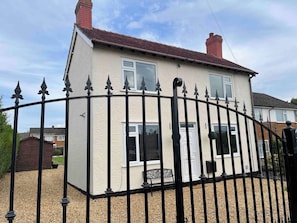 A two-story house with a black metal fence, a white exterior, and a red-tiled roof. - Delightful 2 bed detached home with secure parking (Cannock)