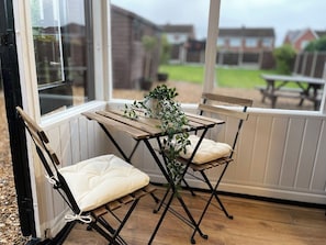 A patio area with two folding chairs and a table, a potted plant, and a view of a residential area through a window. - Delightful 2 bed detached home with secure parking (Cannock)
