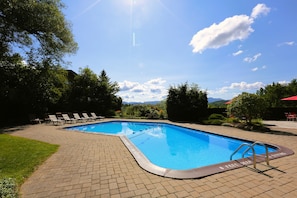 A rectangular swimming pool with a brick deck, surrounded by lounge chairs and trees.