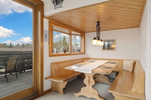 A corner dining area with wooden benches and a table, a large window with a view, and a pendant light fixture.