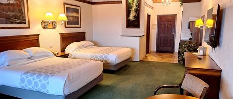 Habitación de hotel con dos camas, techo de madera, alfombra verde, escritorio de madera, una silla y una pequeña mesa.