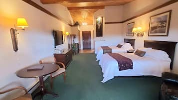 A hotel room with two beds, a desk, a chair, and a television.