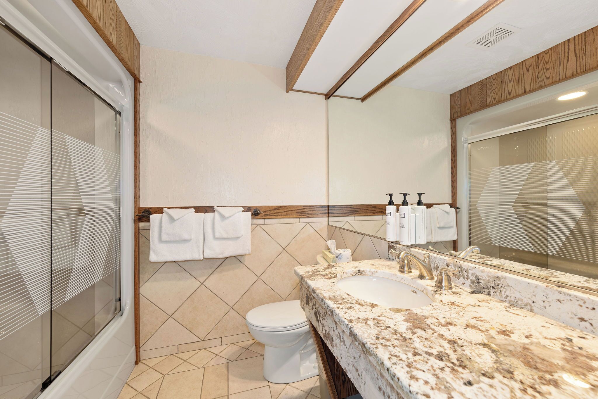 A modern bathroom with a large mirror, a sink, and a toilet. There are towels and toiletries on the wall.
