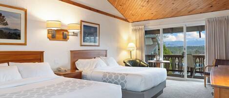 A hotel room with two beds, a wooden ceiling, a balcony with a view, and a painting on the wall.