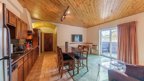 A kitchen with wooden cabinets, a dining area with a table and chairs, a living room with a sofa, and a large sliding glass door leading to a balcony.