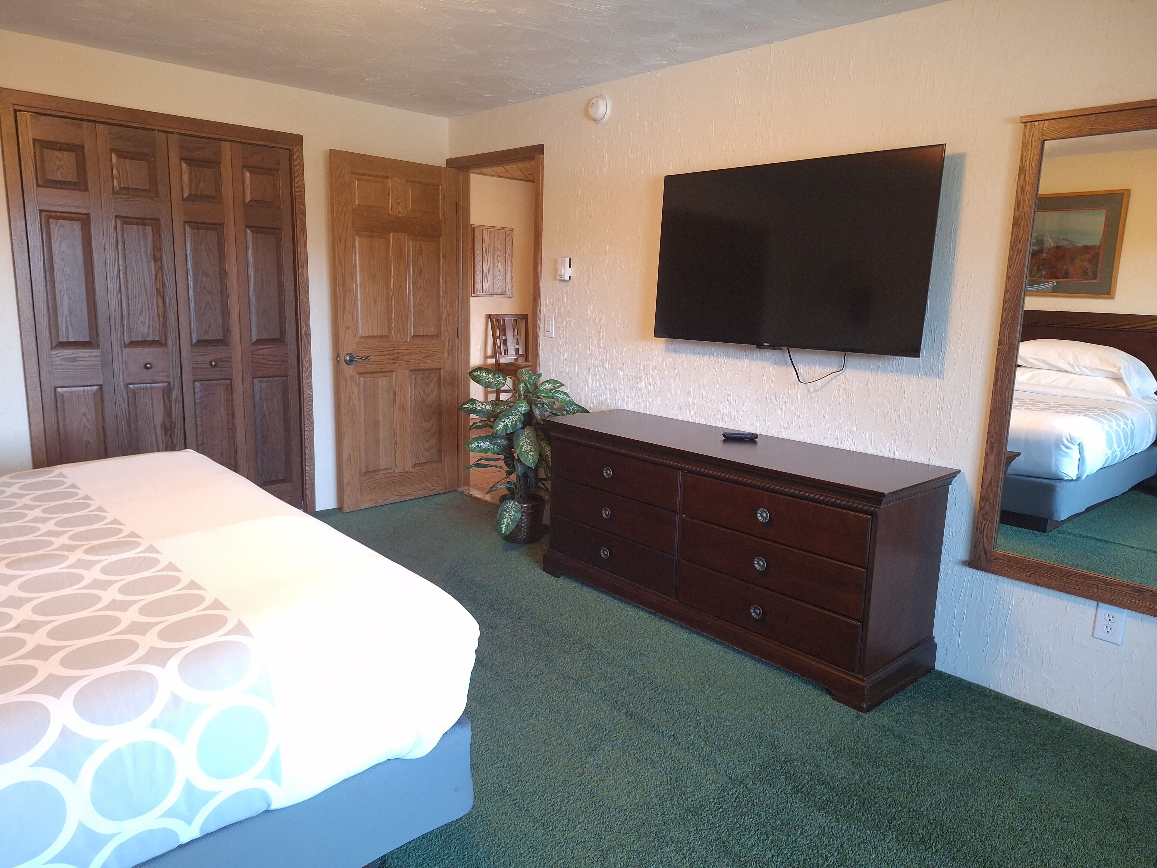A bedroom with a bed, dresser, TV, and a large mirror.