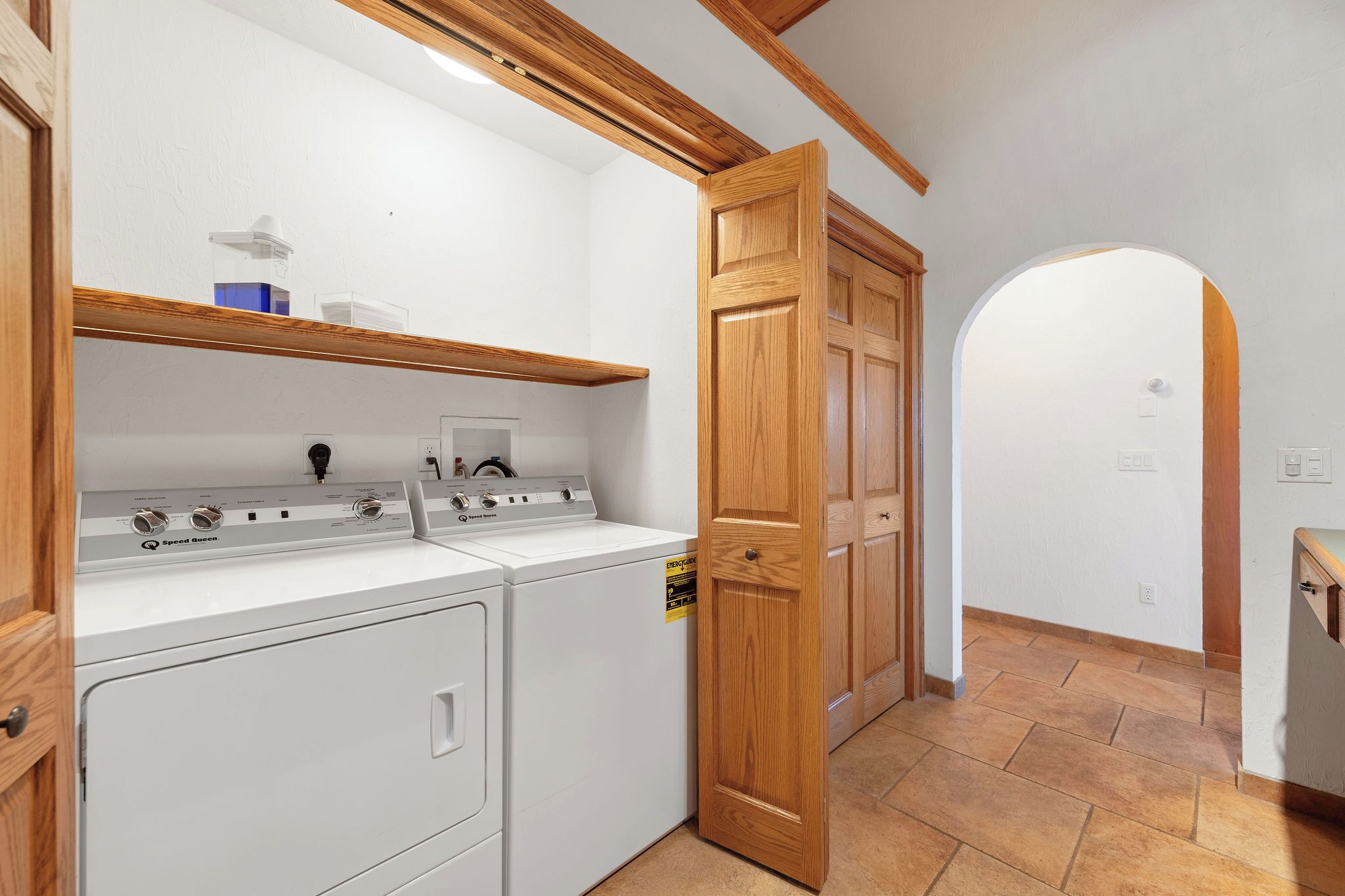 A laundry room with a front-loading washer and dryer, wooden cabinets, and a tiled floor.